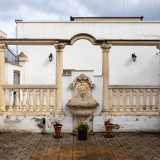 ...mentre a sinistra non passa inosservato un patio classicheggiante con una fontana centrale affiancata da due balaustre